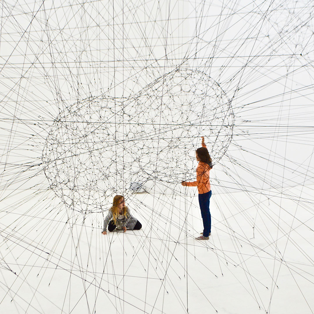 Two young girls sitting amongst numerous interconnected wires