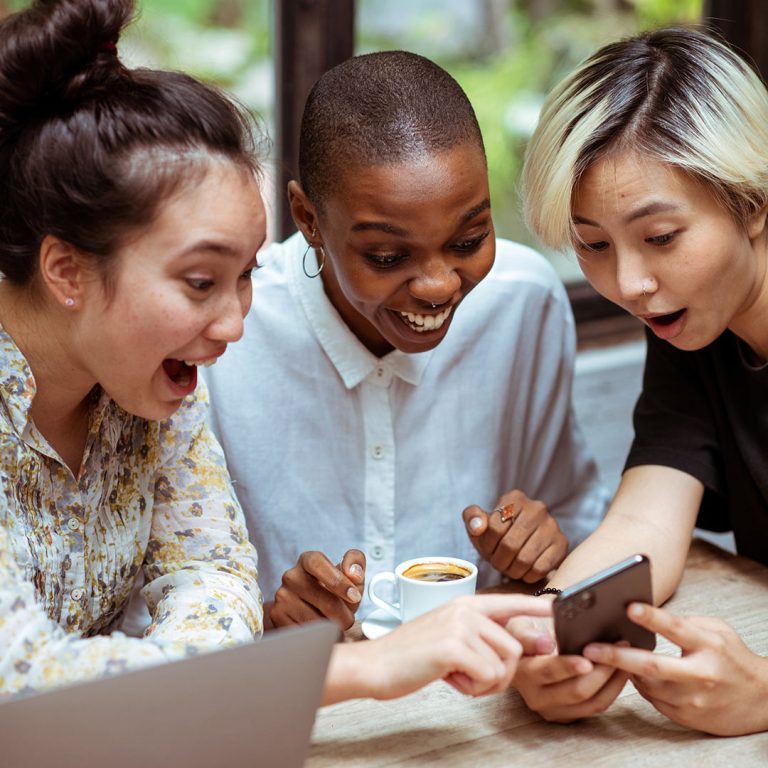 Three women laughing together at something they are seeing on a phone