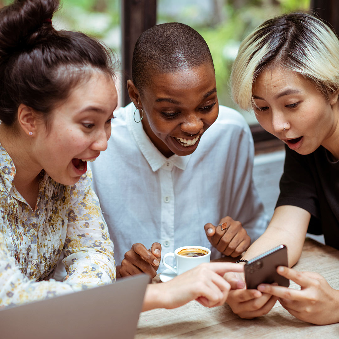 Three women laughing together at something they are seeing on a phone