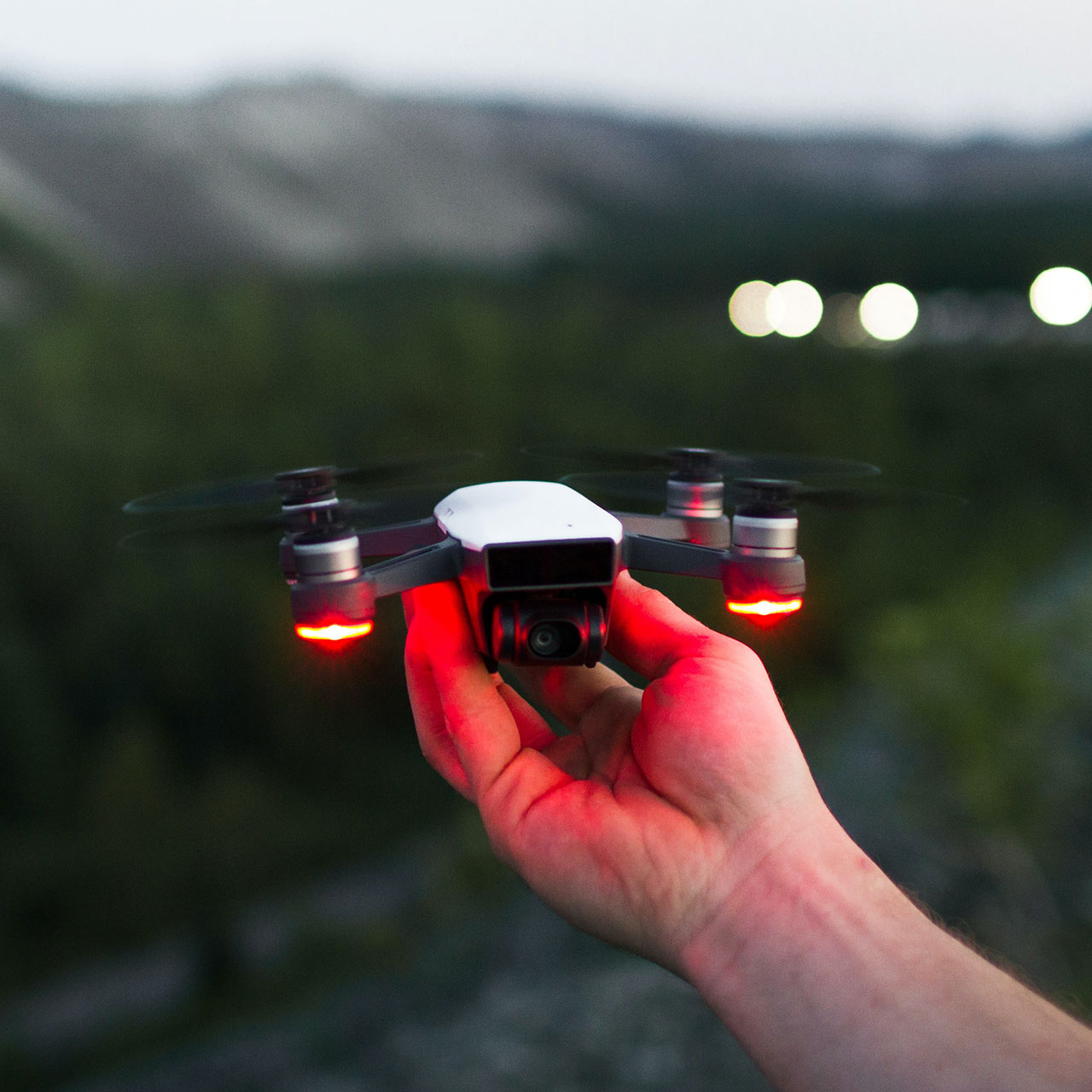 A hand holding a small drone with red landing lights